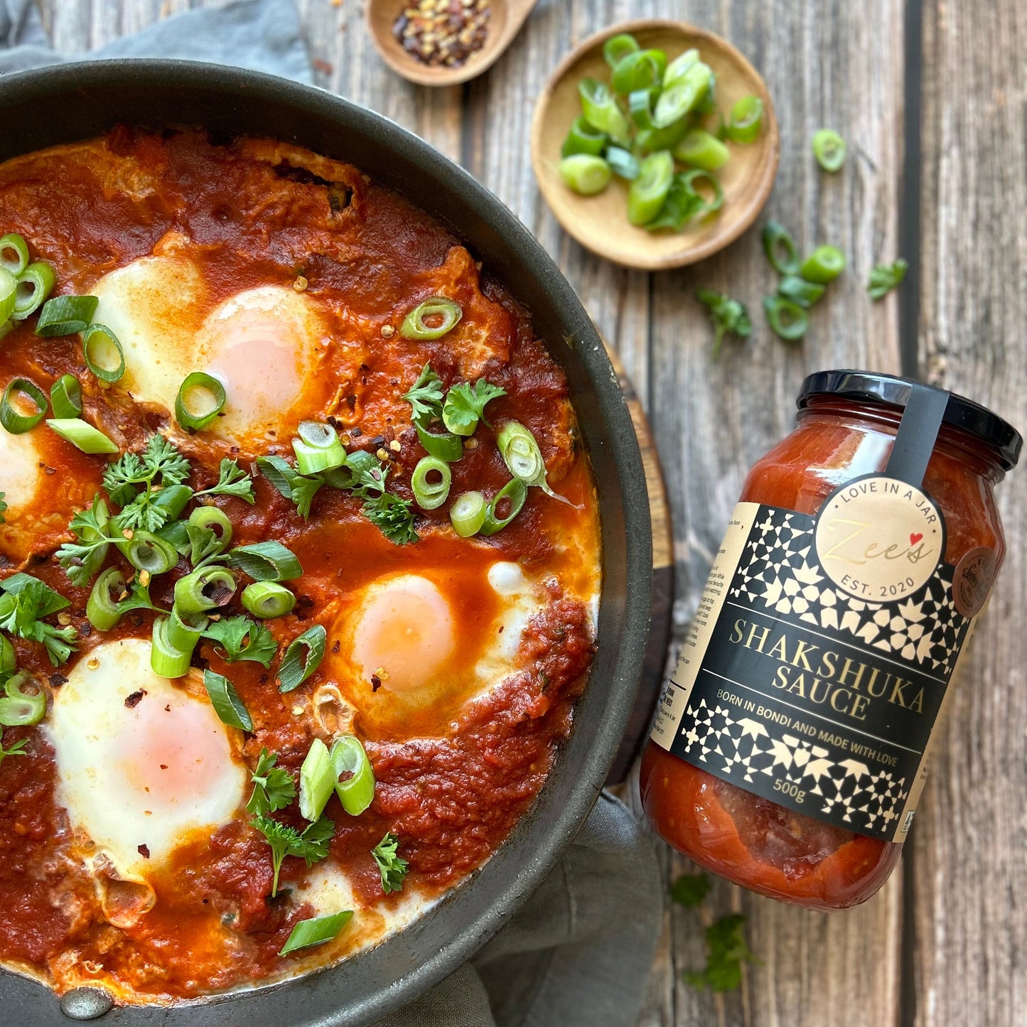 Shakshuka with green onions and a bottle of Shakshuka Sauce on a wooden surface