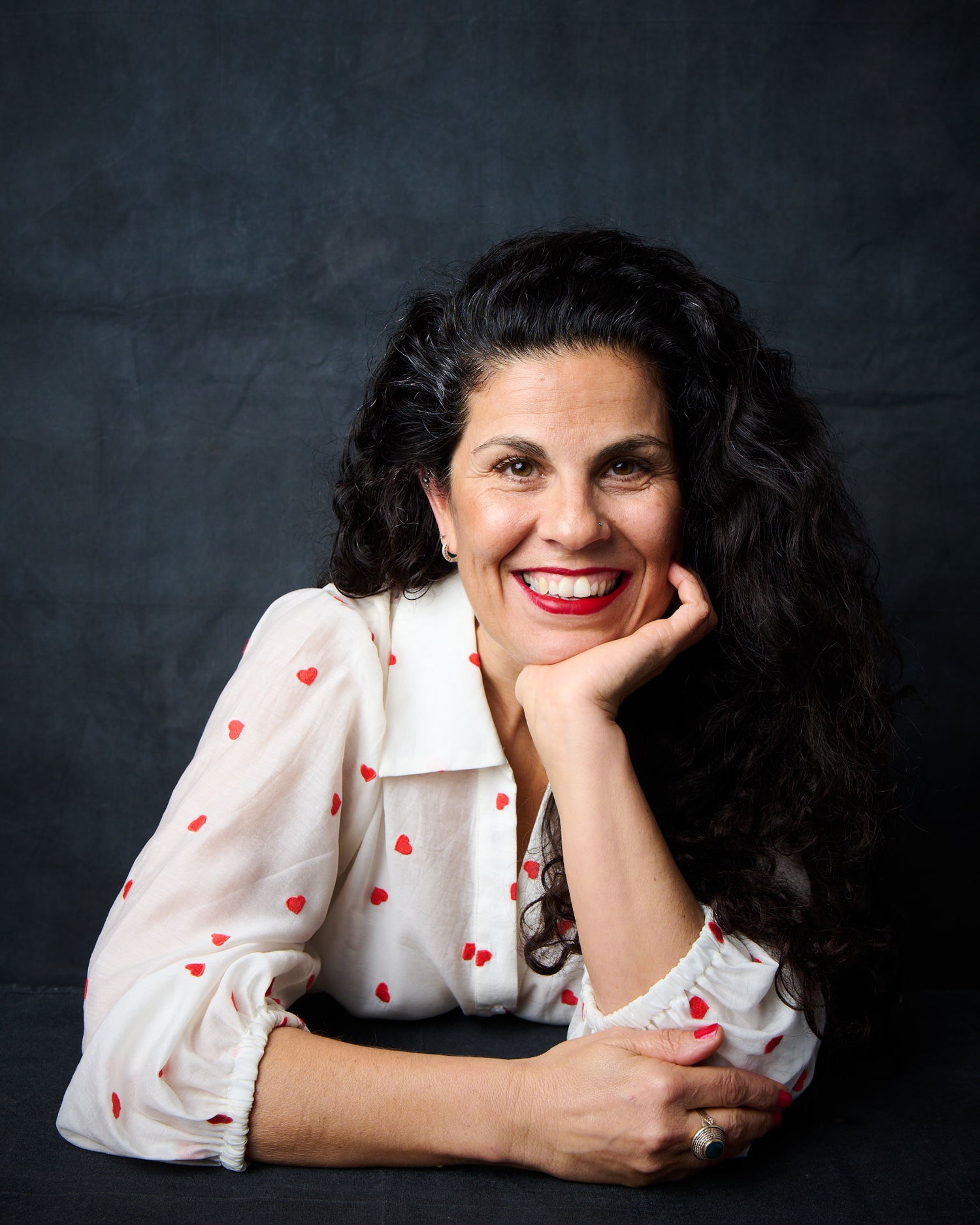 Woman with dark hair and red lipstick wearing a white blouse with red polka dots against a black background